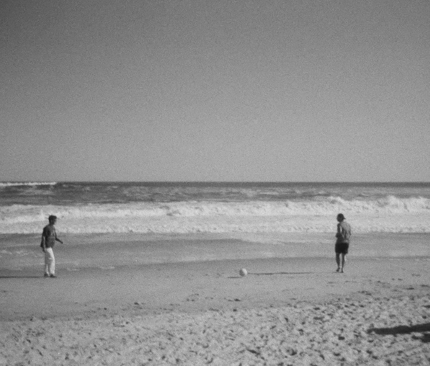 Two people kicking a ball on a black-and-white beach