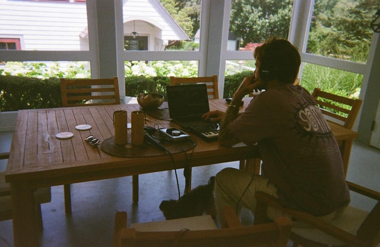A man with headphones making music on a laptop at a porch table