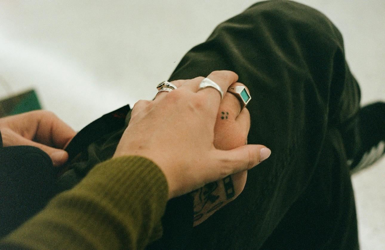 A ringed hand resting on another person’s tattooed hand