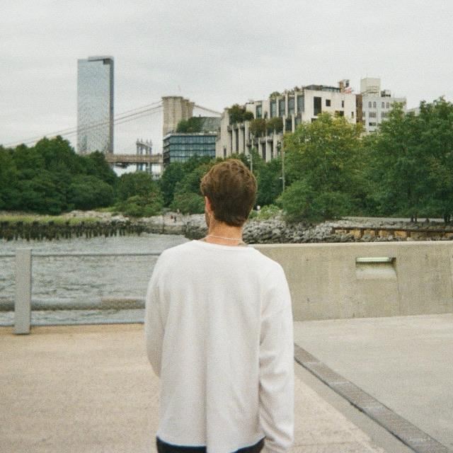 A man in a white sweater looking out over the river toward the city